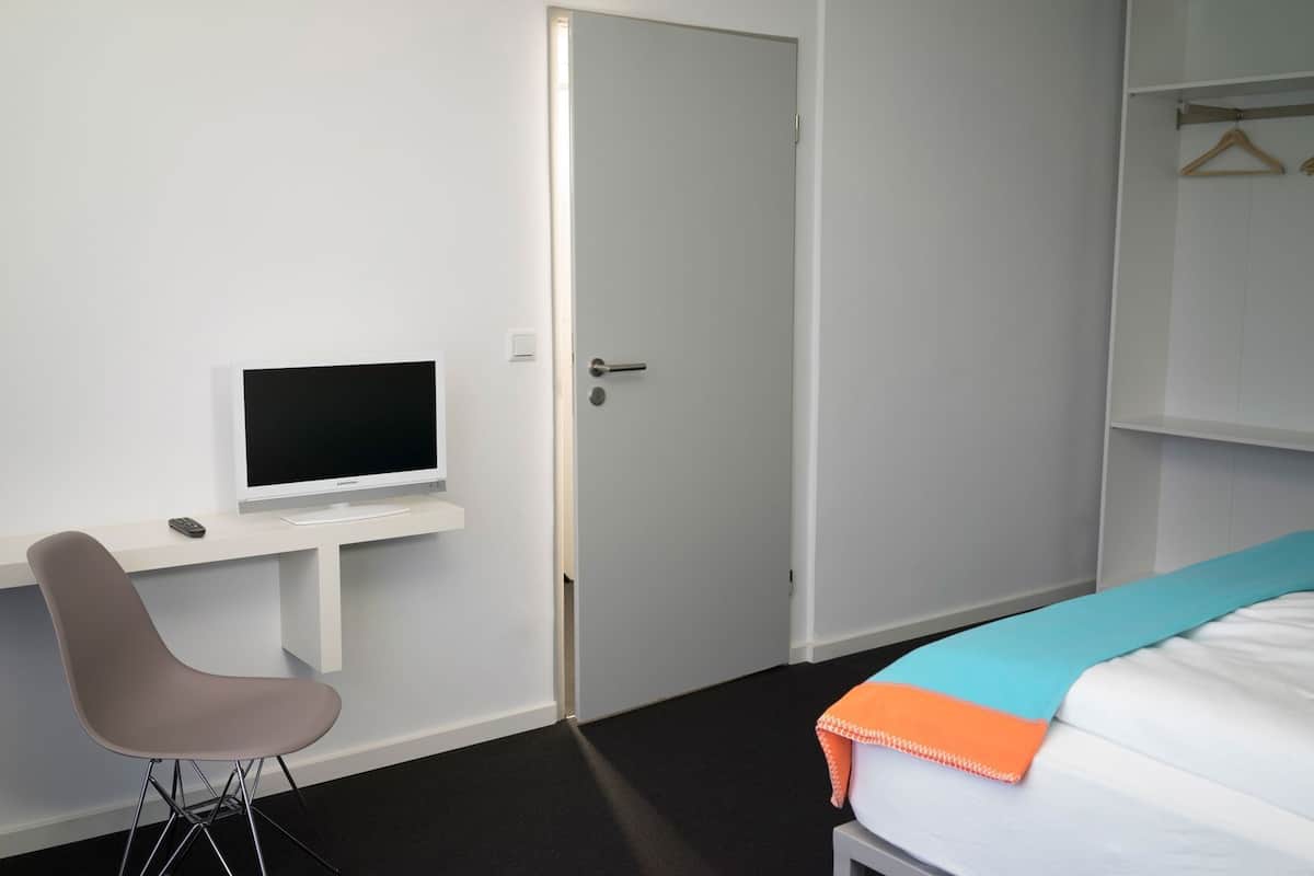 A hotel room with a bed, a desk with a TV, a chair, and a wardrobe.