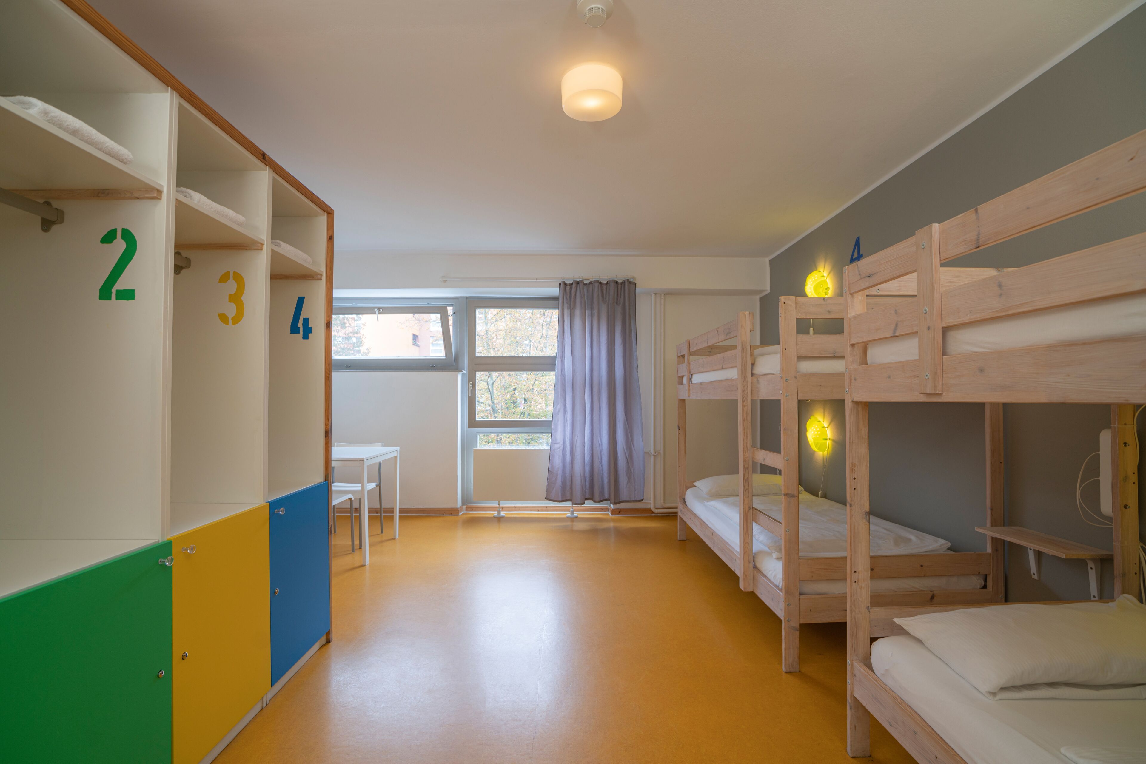 A children's room with bunk beds, a window with curtains, and a white table.
