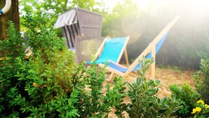 A garden area with a wooden playhouse, a blue lounge chair, and various green shrubs. - BIG MAMA Berlin (Berlin)