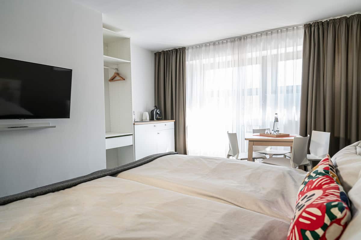 A hotel room with a bed, a desk, a chair, a television, and a window with curtains.