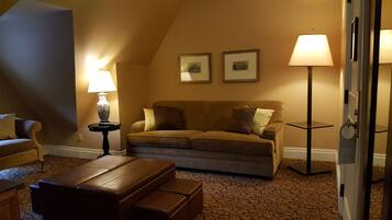A cozy living room with a brown sofa, two framed pictures on the wall, a side table with a lamp, and a patterned carpet.