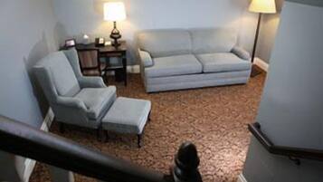 A living room with a light blue armchair, a sofa, and a small table with a lamp.