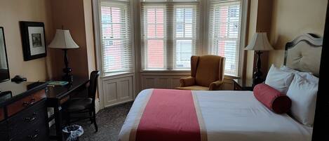 A hotel room with a large bed, a desk, a chair, and a window with blinds.