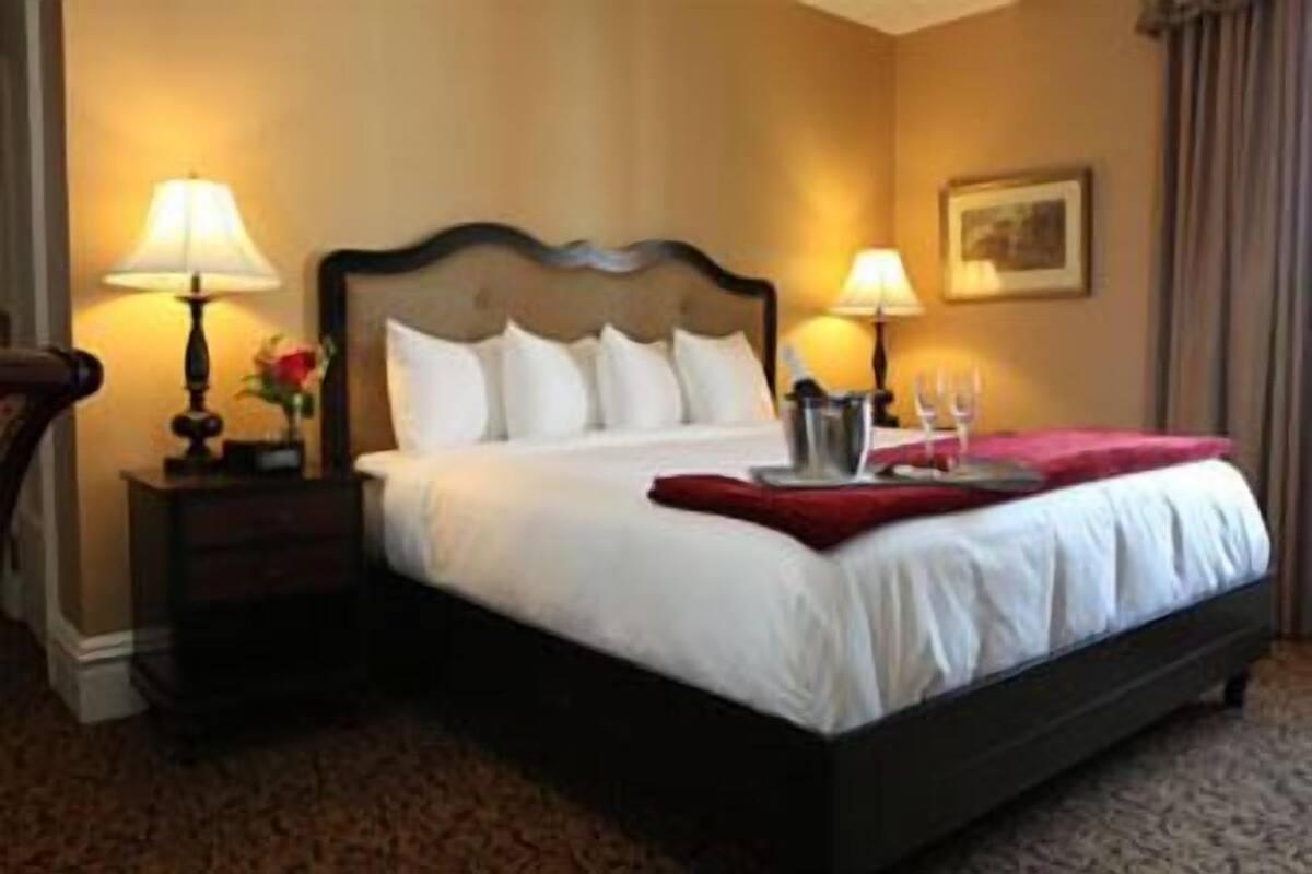 A hotel room with a large bed, two bedside tables with lamps, a red throw blanket, and a framed picture on the wall.