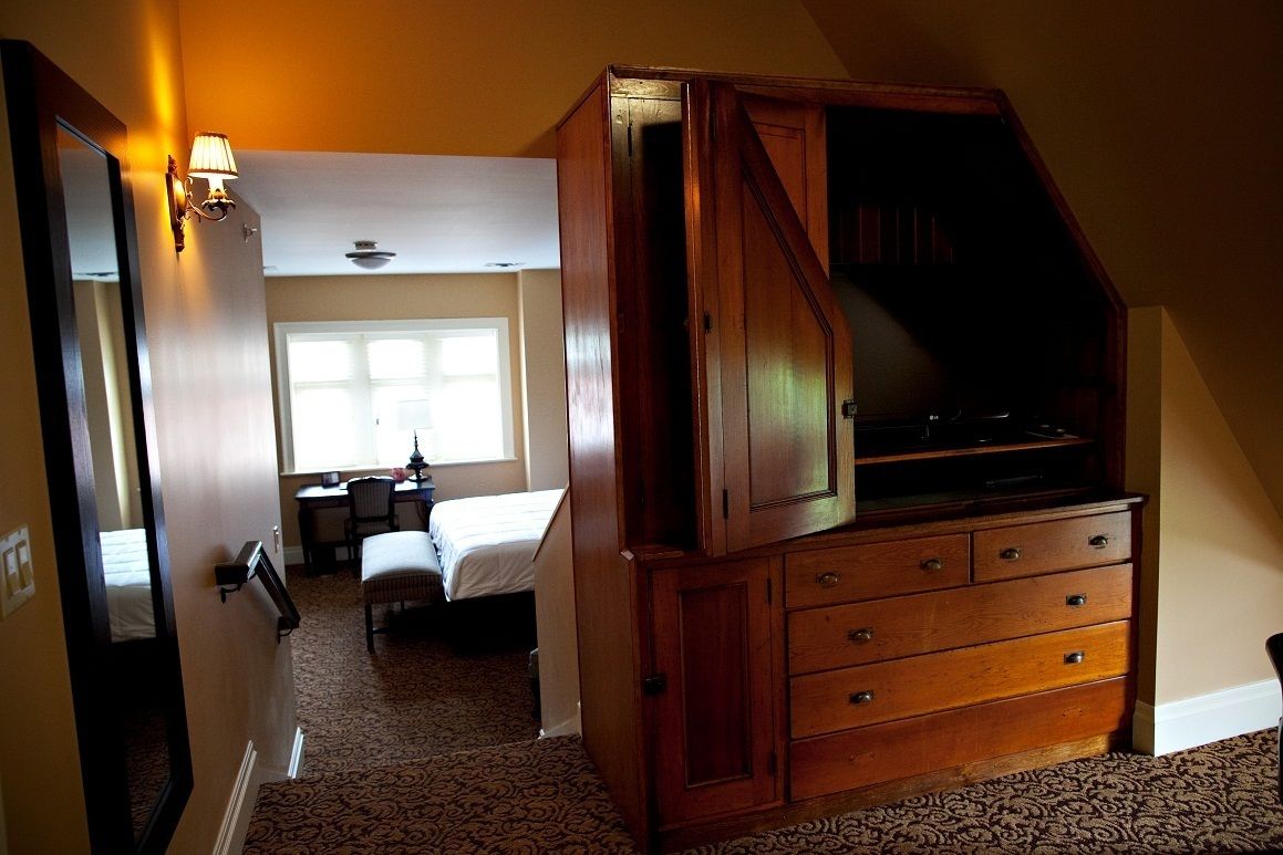 Una habitación de hotel con un gran aparador de madera, una cama, un escritorio y una silla.