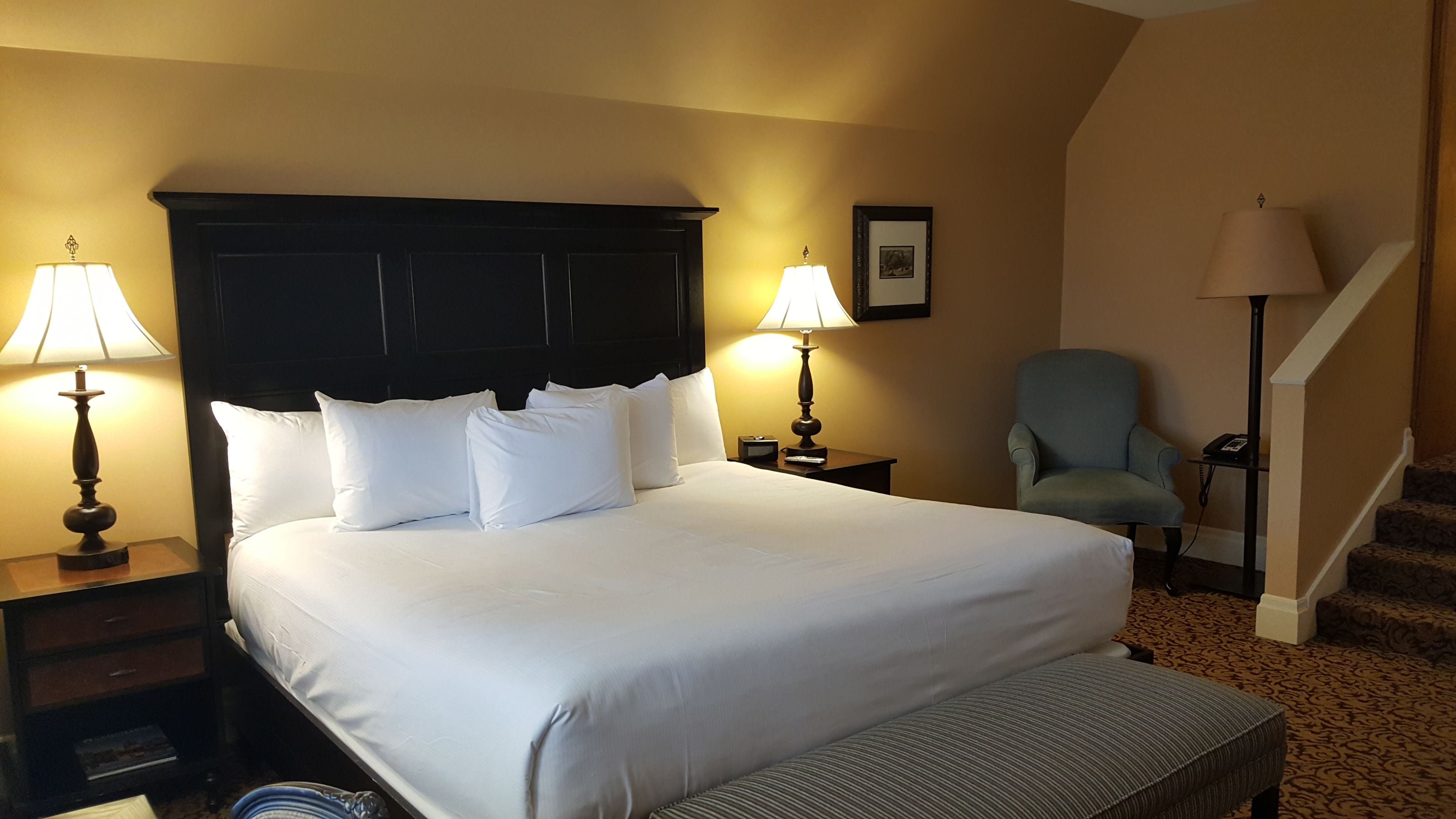 Une chambre d’hôtel avec un grand lit, deux tables de chevet avec des lampes, une chaise et un escalier.
