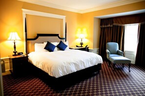 Classic hotel room with a large bed, patterned carpet, and a window with curtains.