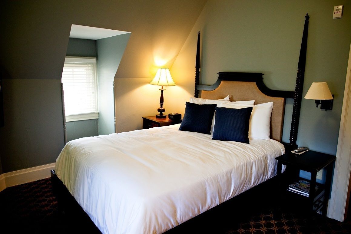 A neatly made bed with white linens, a dark wooden headboard, and a nightstand with a lamp.