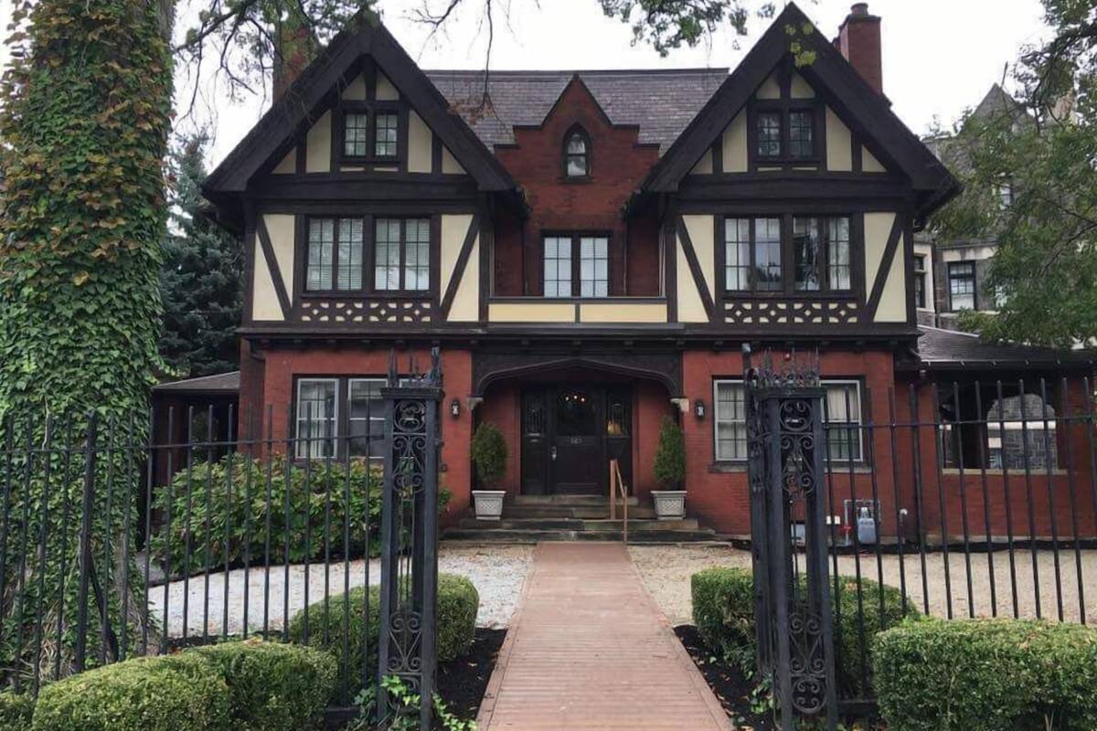 A traditional Tudor-style house with a symmetrical facade, a central entrance with a wooden door, and a brick chimney.