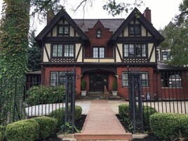 A traditional Tudor-style house with a symmetrical facade, a central entrance with a wooden door, and a brick chimney.