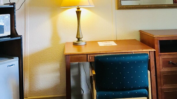 A hotel room with a desk, chair, lamp, television, and a mirror. - Granada Inn Motel (Kalkaska)