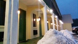A motel with a covered porch and multiple rooms, each with a door and a window. - Granada Inn Motel (Kalkaska)