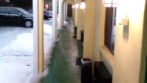 A corridor with a green floor, white walls, and yellow arches. There are lights along the corridor and a car parked outside. - Granada Inn Motel (Kalkaska)
