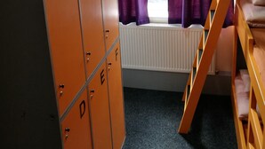 A dormitory room with orange lockers labeled A to E, a window with purple curtains, a white radiator, and a wooden bunk bed. - Birmingham Central Backpackers - Hostel (Birmingham)