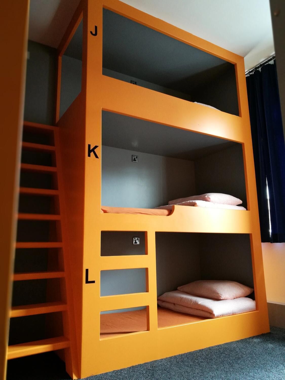 A bunk bed with a ladder on the left, a power outlet on the middle shelf, and a storage compartment on the bottom shelf.