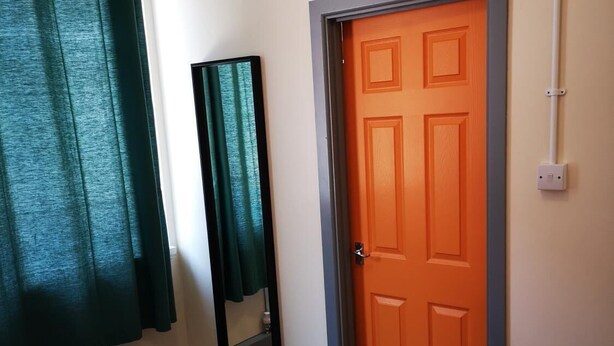 A bedroom with a bed, a door, a mirror, and a light switch on the wall. - Birmingham Central Backpackers - Hostel (Birmingham)