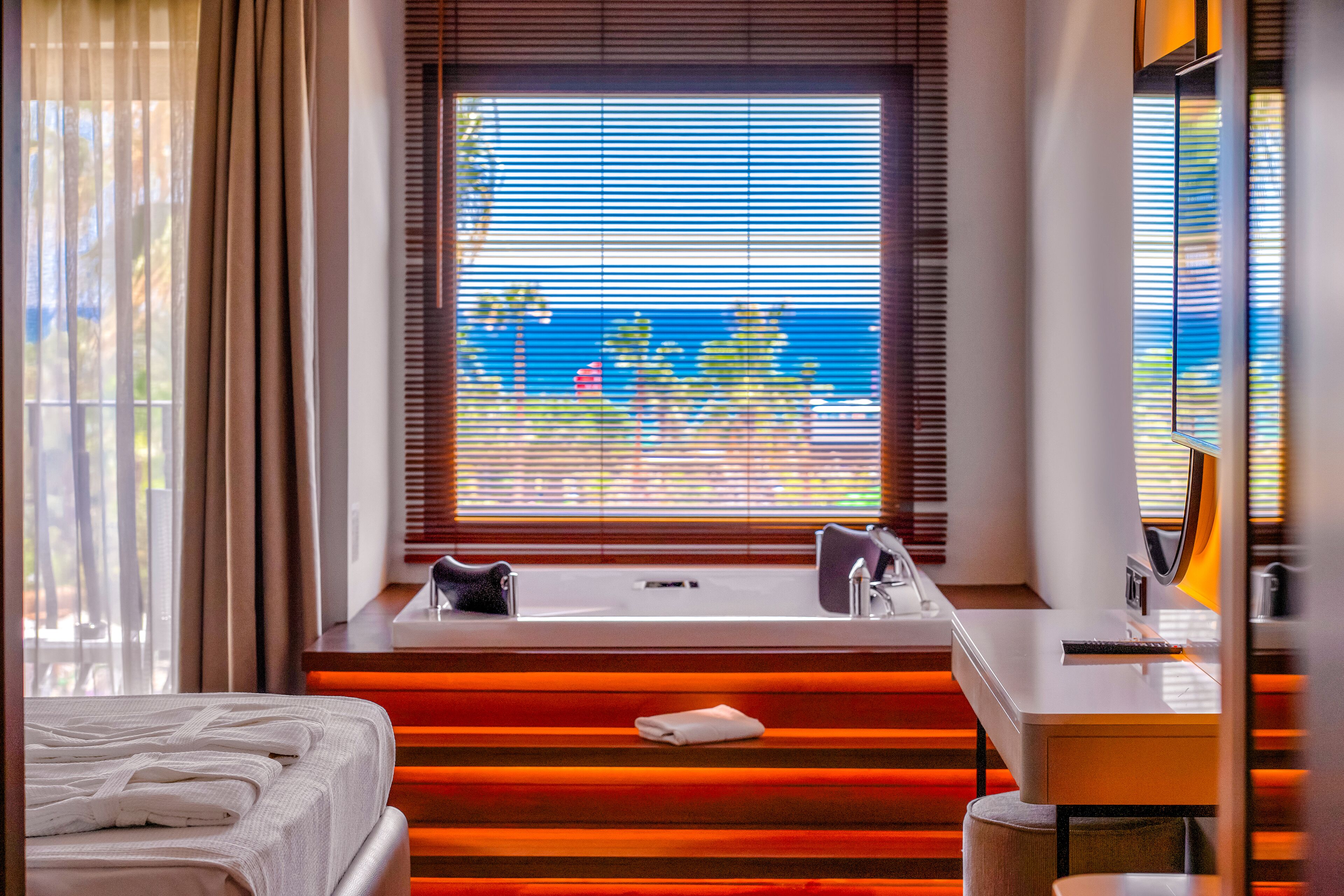 Ett modernt hotellrum med ett stort fönster, en säng, ett skrivbord och ett badkar.