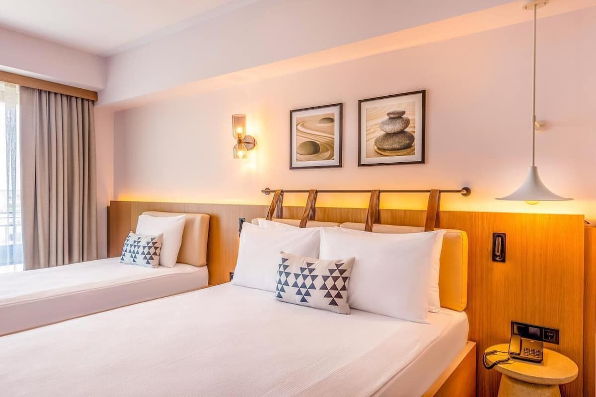 A hotel room with two beds, a bedside table with a phone, and wall-mounted artwork.