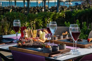 A dining table with a variety of food items and glasses of wine, set against a backdrop of a pool and greenery.