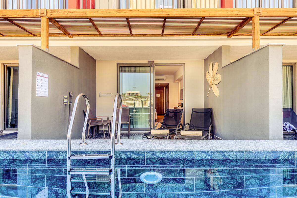 A hotel pool area with a clear view of the pool, lounge chairs, and a wooden pergola overhead.