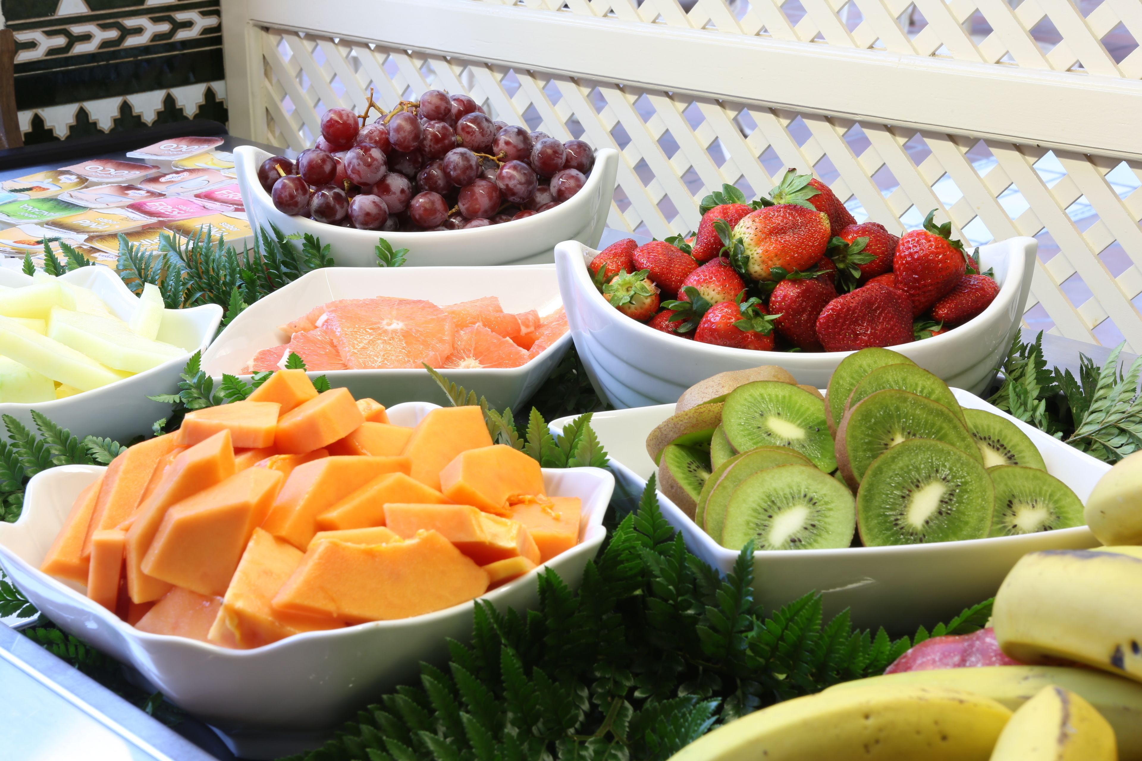 A fruit display with bowls of grapes, strawberries, kiwi, cantaloupe, and oranges.