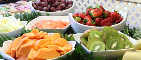 En fruktuppsättning med skålar fyllda med vindruvor, jordgubbar, kiwi, honungsmelon och apelsiner.