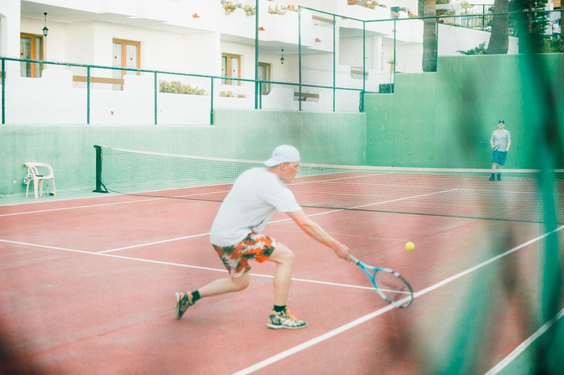 Een tennisbaan met een net, een stoel en een gebouw op de achtergrond.