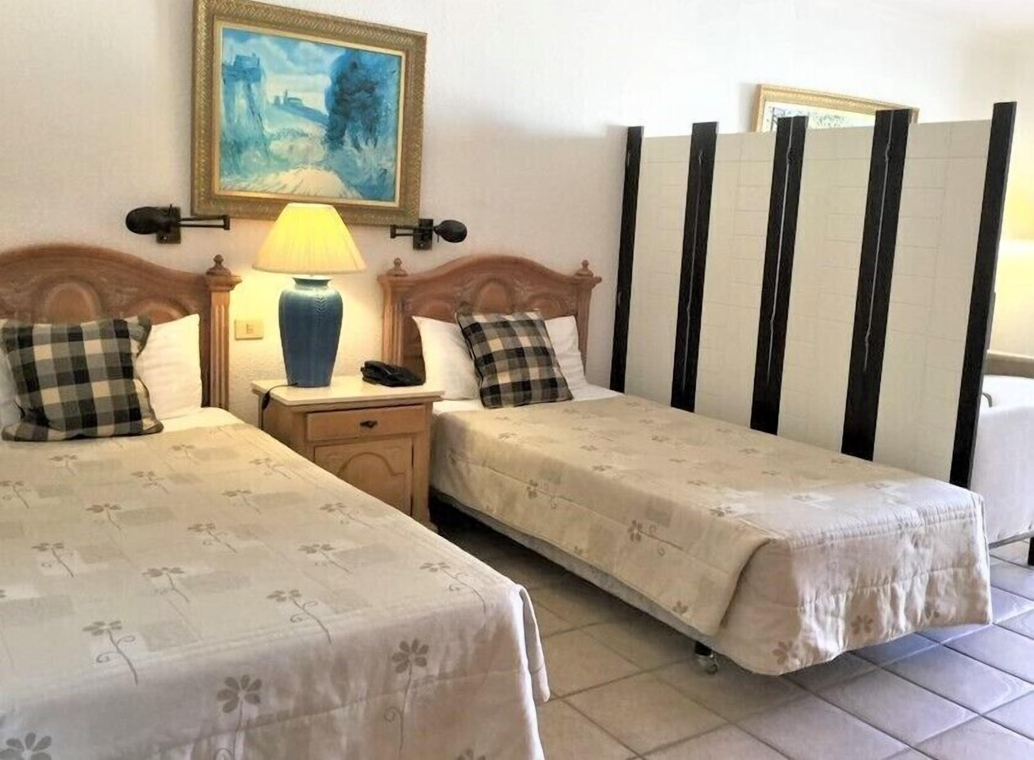 Une chambre d’hôtel avec deux lits, une table de chevet avec une lampe, un tableau au mur et une cloison à rayures.