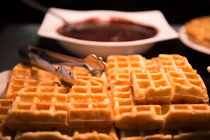 Primer plano de un plato de waffles dorados y crujientes, acompañado de un tazón de almíbar y un par de pinzas.