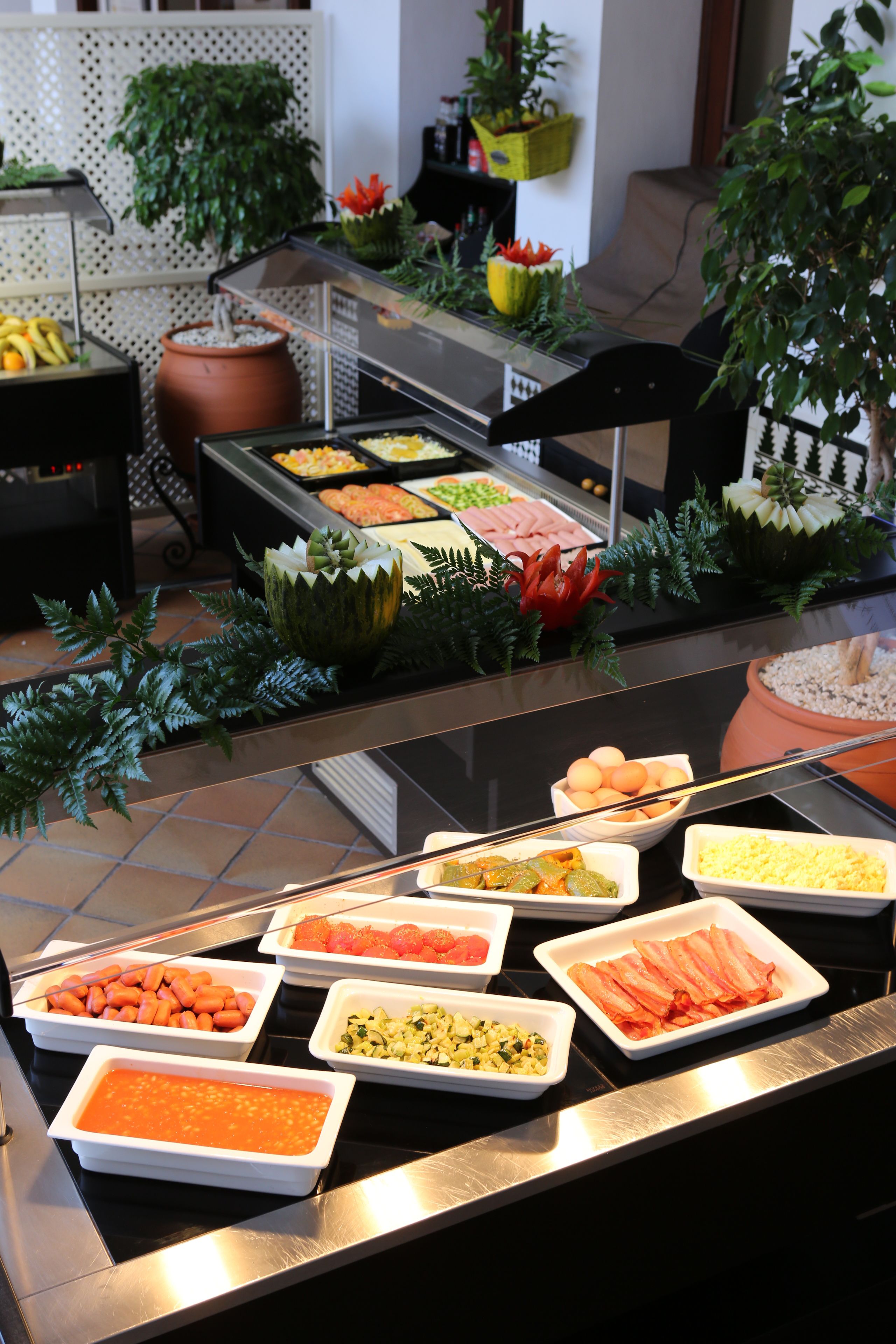 A buffet with various food items and decorative plants.