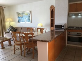 Uma cozinha compacta com micro-ondas, fogão e um espaço de refeições com cadeiras e mesa de madeira.