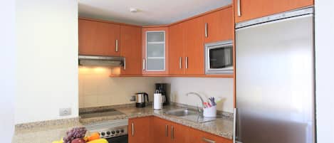 A kitchen with wooden cabinets, a stainless steel refrigerator, a microwave, a stove, and a fruit bowl on the counter.