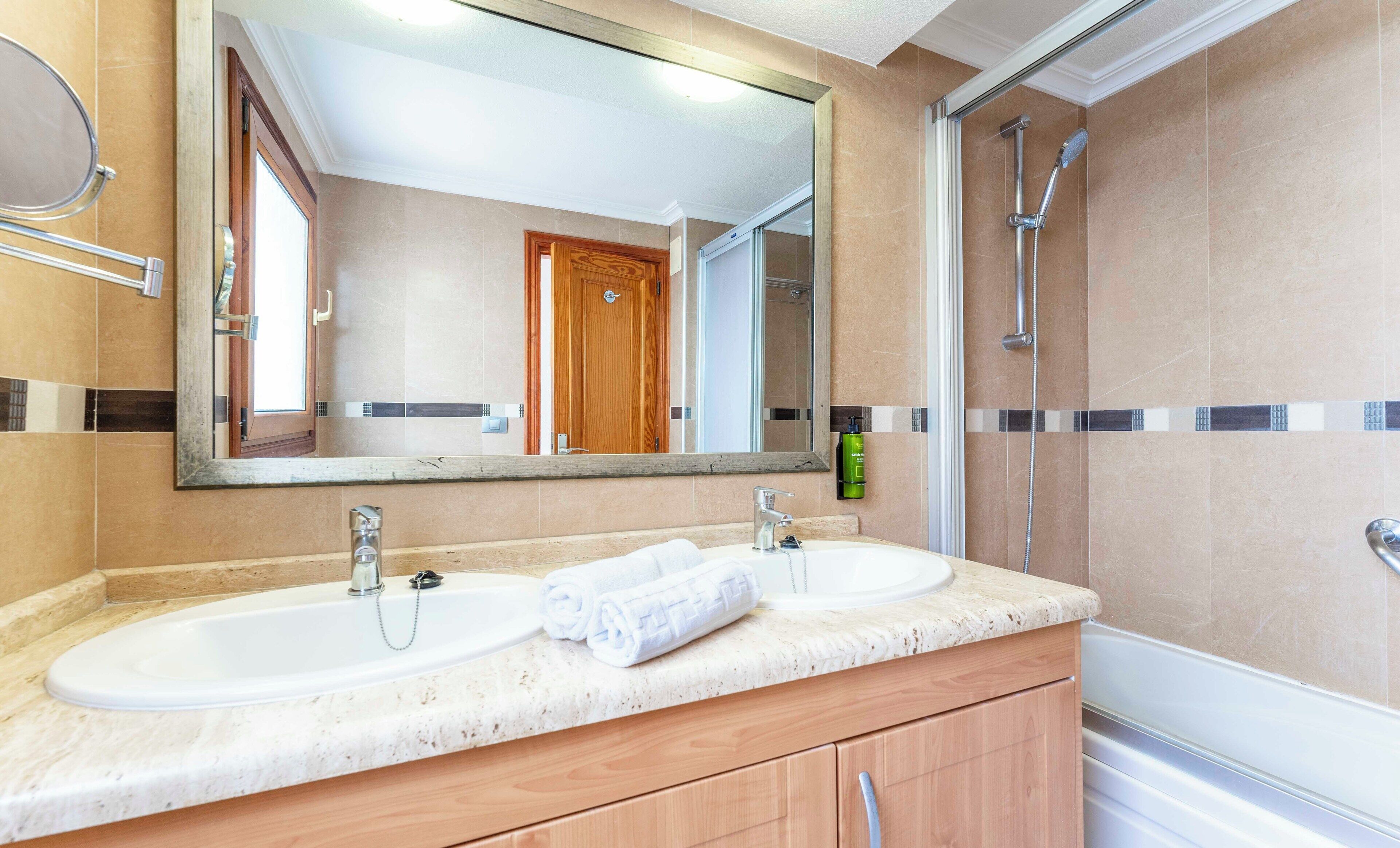 A bathroom with two sinks, a large mirror, and a shower.