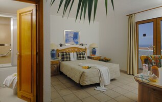 Habitación de hotel con cama, mesitas de noche, ventana con cortinas y baño con bañera, con vista al mar.