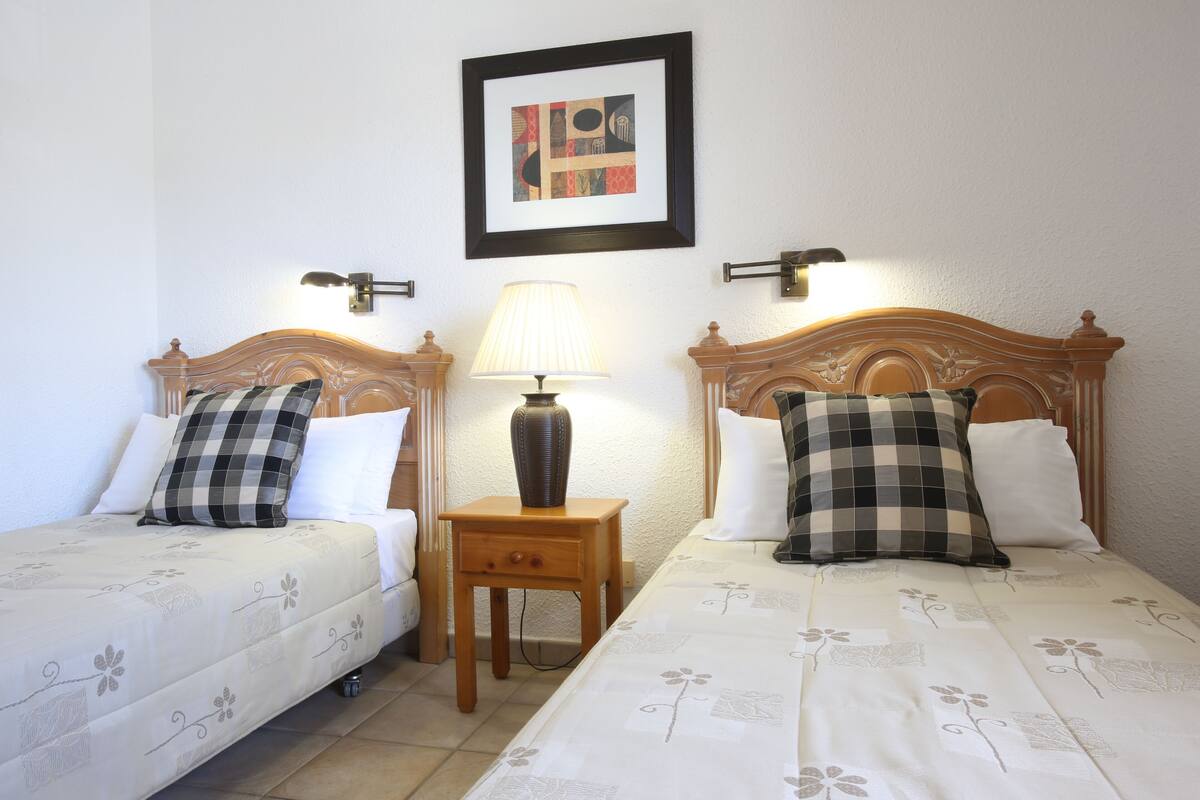 A double bed with a wooden headboard, a bedside table with a lamp, and a framed picture on the wall.