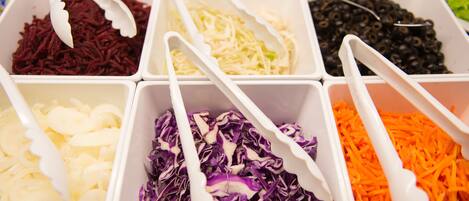 A variety of shredded vegetables in white containers with white plastic tongs.