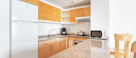 A compact kitchen with a refrigerator, coffee maker, microwave, and wooden chairs.