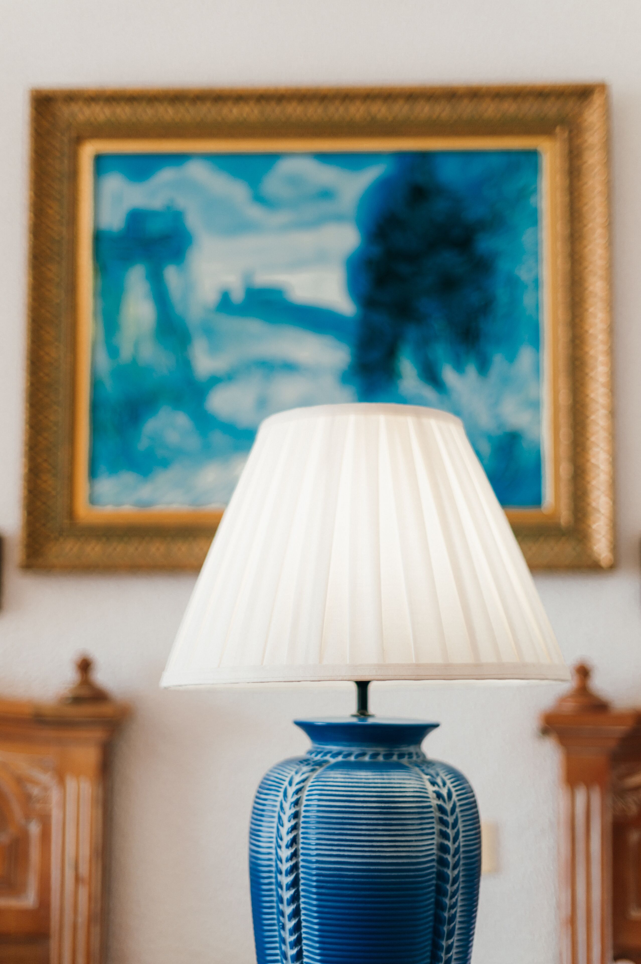 A blue vase lamp with a white lampshade on a table.