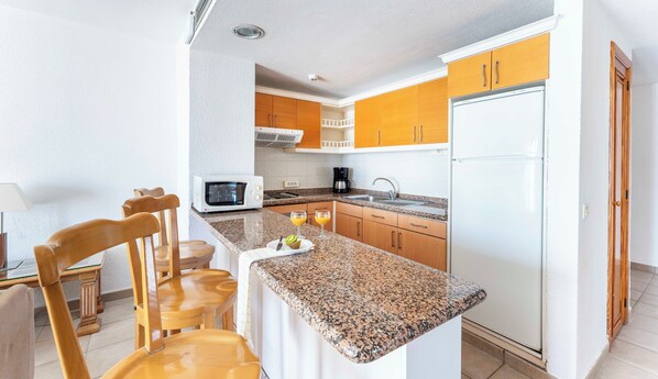 A compact kitchen with granite countertops, wooden cabinets, a microwave, a coffee maker, and a refrigerator.