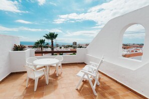 A terrace with a white table and chairs, a view of the city, and a palm tree.