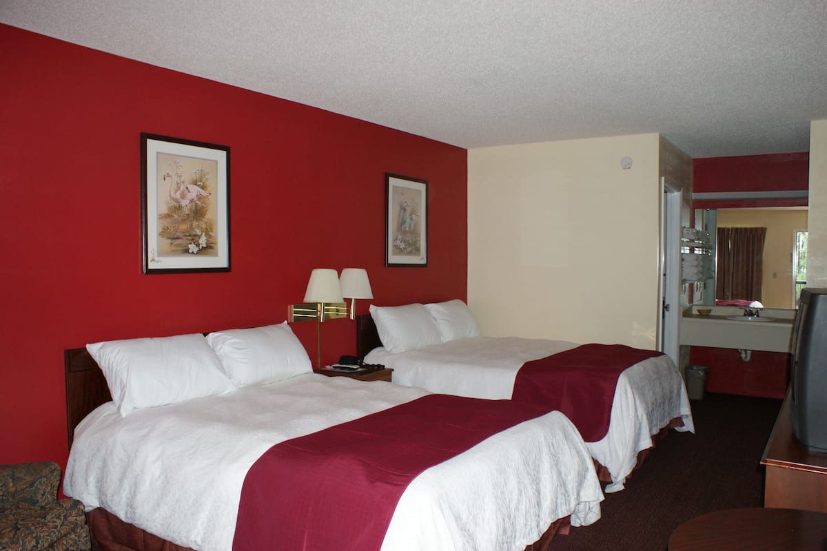 A hotel room with two beds, a television, and a bathroom visible through an open door.