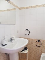 Un bagno con un lavandino bianco, uno specchio e un portasciugamani.