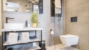 Un baño moderno con cabina de ducha de vidrio, inodoro blanco, lavamanos de mármol y toallero.