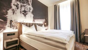A hotel room with a large wall mural of a llama, a bed with white linens, a bedside table, and a chair.