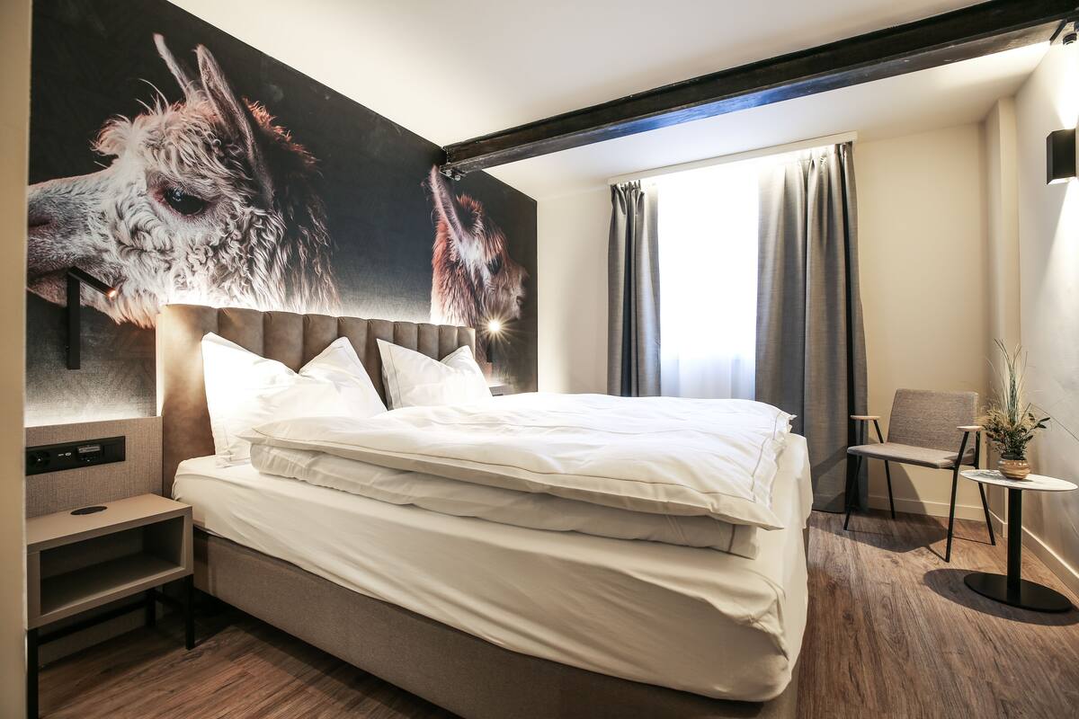 A modern hotel room with a large bed, a nightstand, a chair, and a small table.