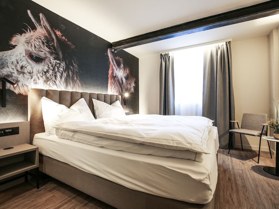 Una habitación de hotel moderna con una cama grande, una mesita de noche, una silla y una pequeña mesa.