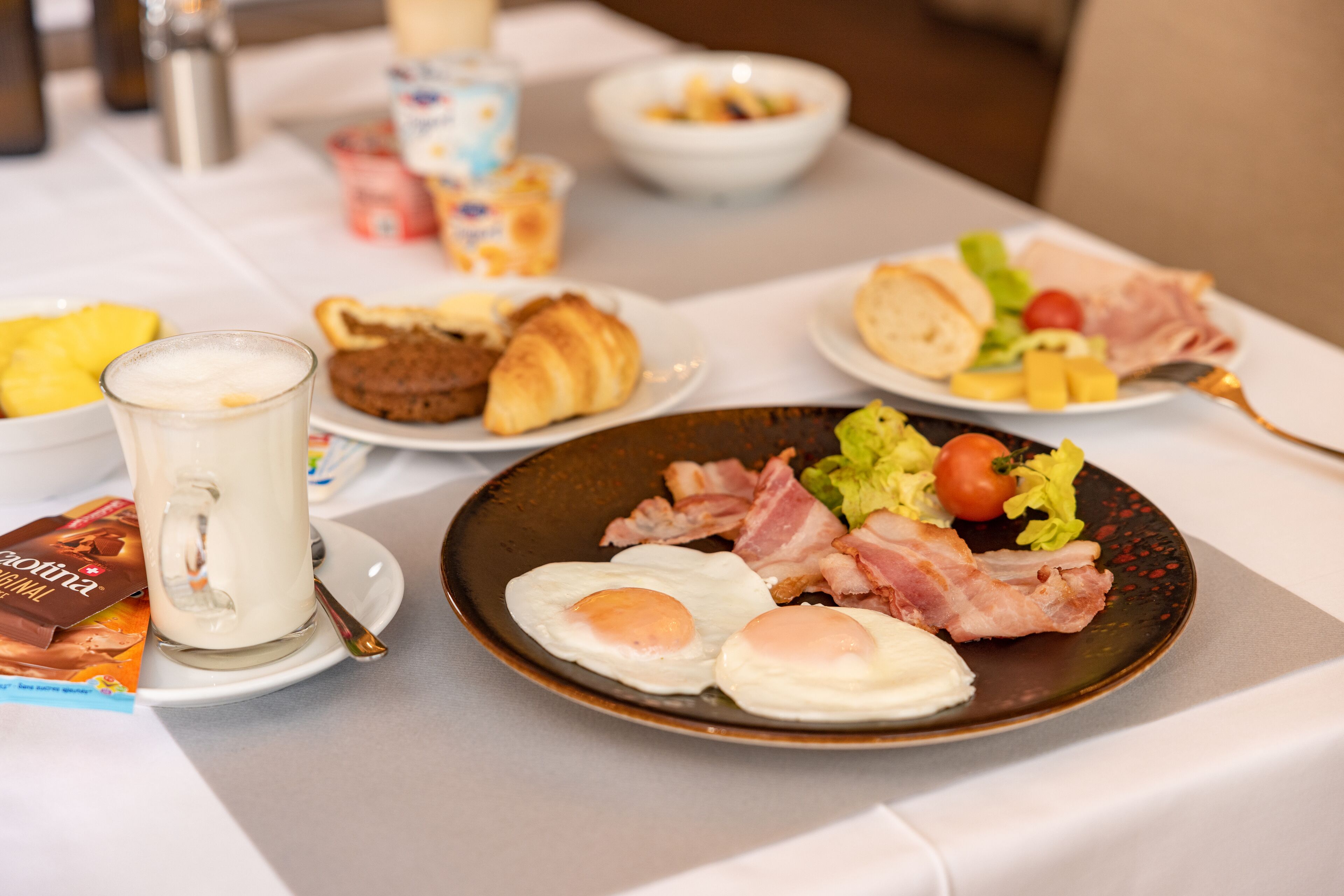 Una mesa de desayuno con platos de huevos, tocino, tostadas y fruta.
