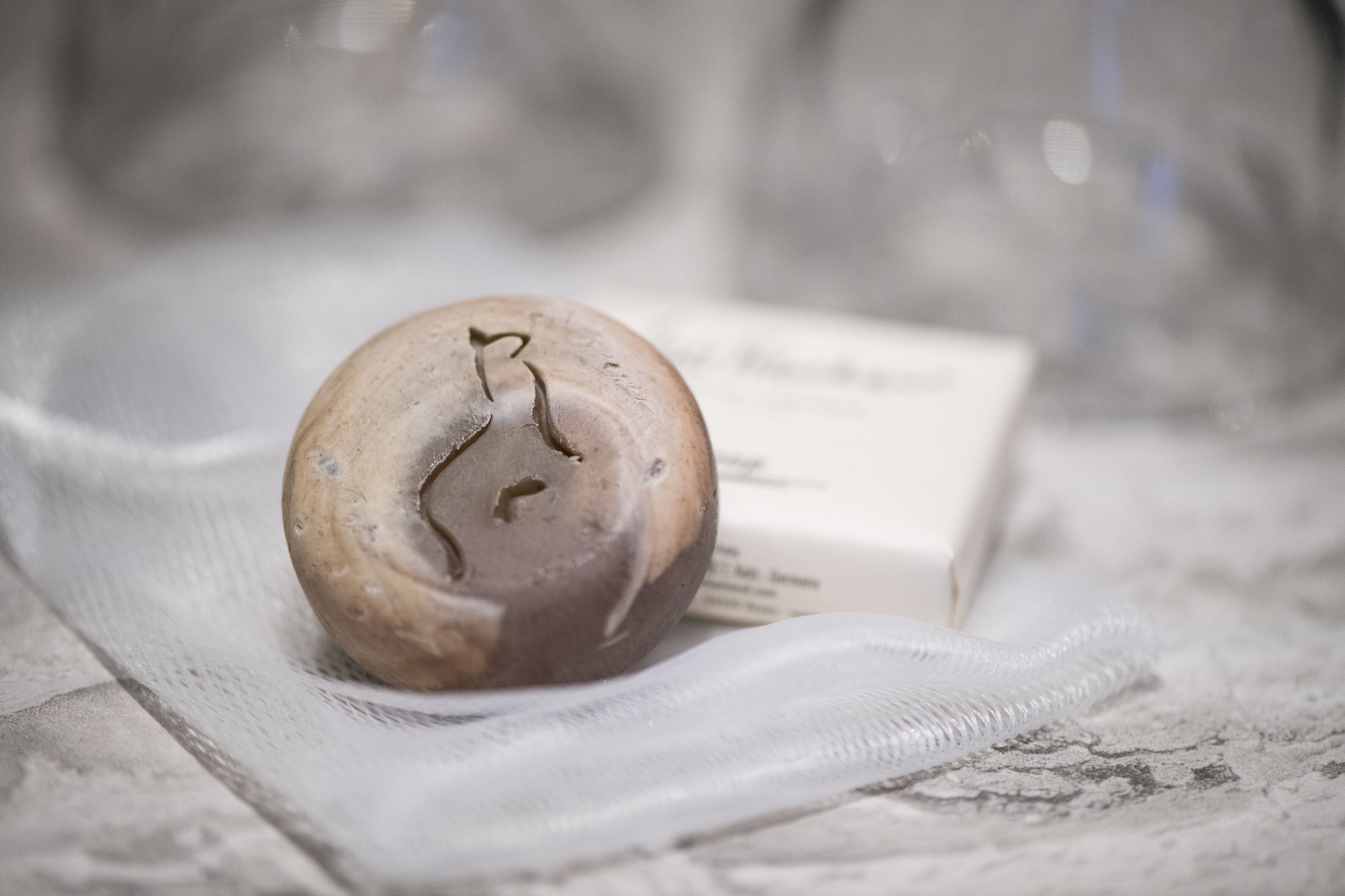 A candle with a heart design on a textured surface, possibly a tablecloth, with a blurred background.