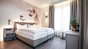 Habitación de hotel moderna con una cama grande, una mesita de noche y una lámpara de pared. Cuenta con ventana con cortinas.