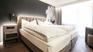 Una habitación de hotel moderna con una cama grande, una mesita de noche, un panel de control en la pared y un ventanal con cortinas.